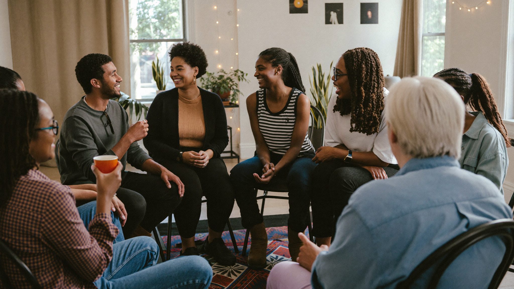 A diverse peer support group sitting together, talking and laughing in a bright community room.
